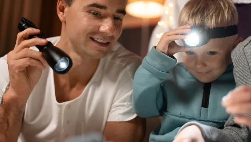 Padre e hijo usando linternas durante un apagón, en un ambiente familiar y acogedor.